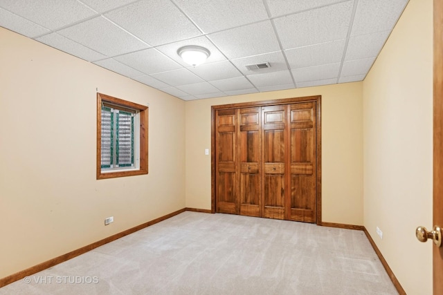 unfurnished bedroom featuring a drop ceiling and light colored carpet