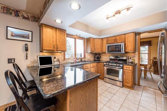 kitchen featuring appliances with stainless steel finishes, a kitchen bar, decorative backsplash, kitchen peninsula, and dark stone counters