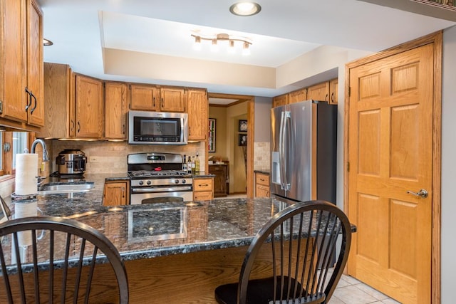 kitchen with appliances with stainless steel finishes, sink, dark stone countertops, decorative backsplash, and kitchen peninsula