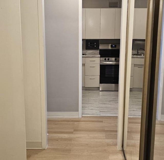 kitchen featuring stainless steel electric range oven, sink, light hardwood / wood-style floors, and white cabinets