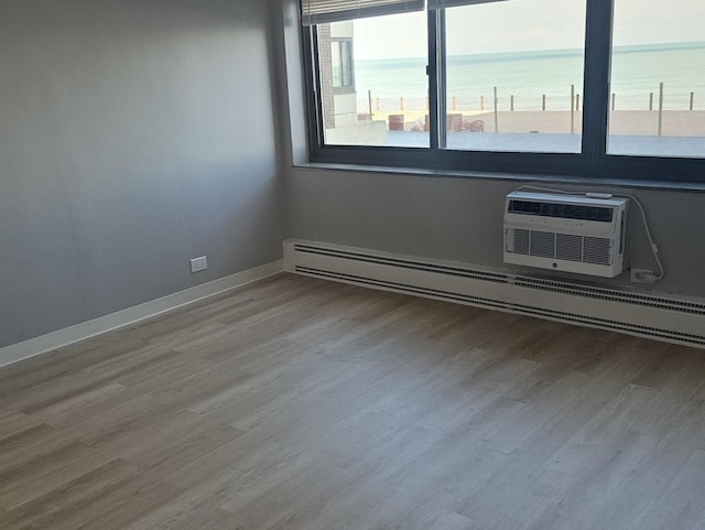 unfurnished room with a wall mounted air conditioner, wood-type flooring, baseboard heating, and a water view