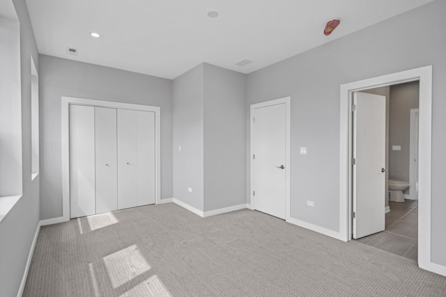 unfurnished bedroom with light colored carpet, a closet, and ensuite bathroom