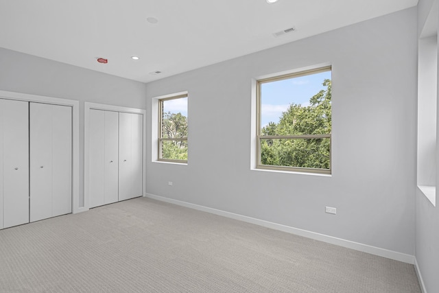 unfurnished bedroom featuring two closets and light carpet