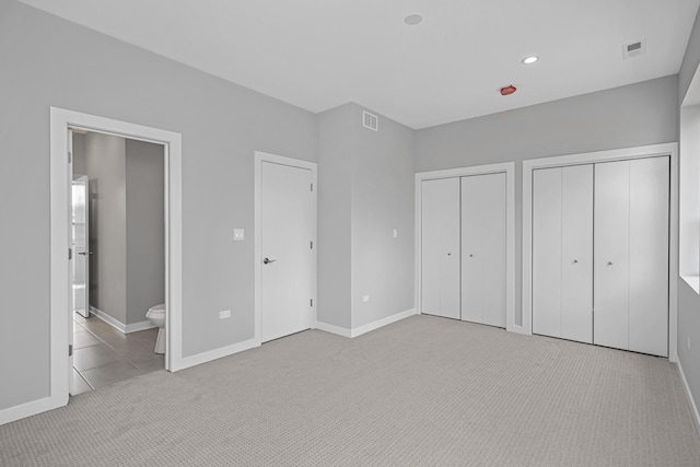 unfurnished bedroom with ensuite bathroom, two closets, and light colored carpet