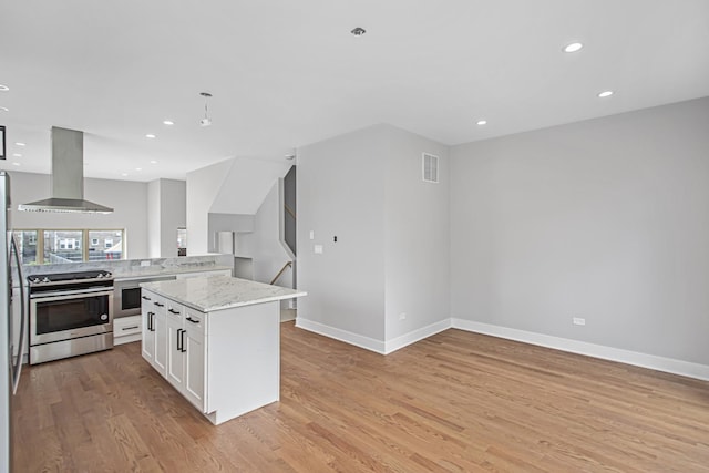 kitchen featuring white cabinetry, light stone counters, light hardwood / wood-style flooring, appliances with stainless steel finishes, and wall chimney range hood