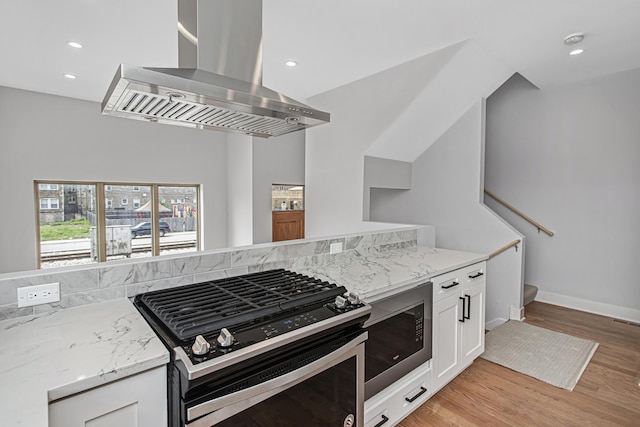 kitchen with built in microwave, white cabinets, exhaust hood, stainless steel range with gas stovetop, and light hardwood / wood-style flooring