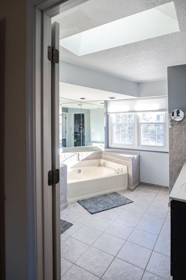 bathroom with a skylight, a textured ceiling, vanity, tile patterned flooring, and a washtub