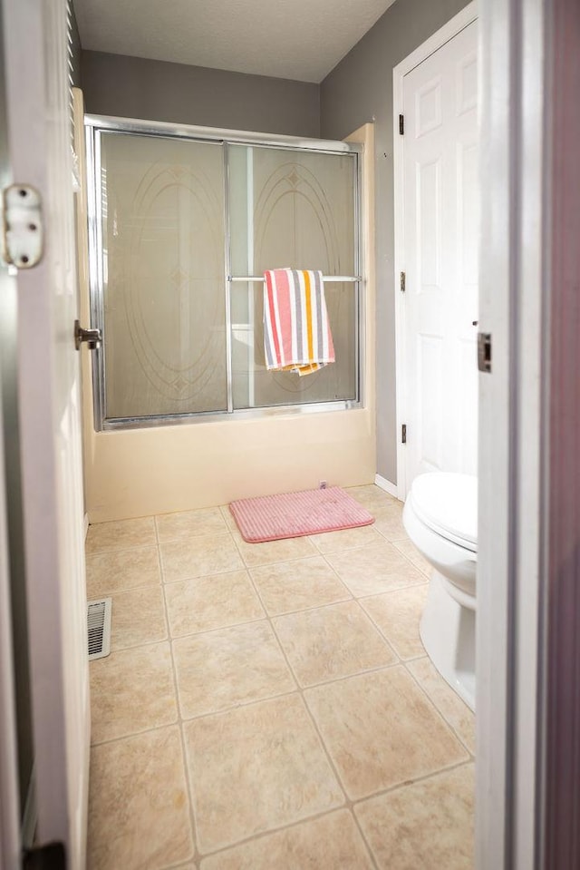 bathroom featuring bath / shower combo with glass door, tile patterned floors, and toilet