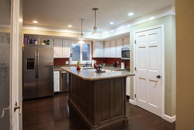 kitchen featuring dark wood-type flooring, crown molding, a center island, hanging light fixtures, and appliances with stainless steel finishes