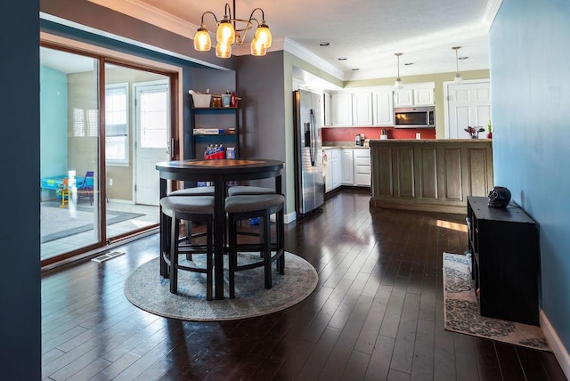 dining area featuring dark wood-type flooring, ornamental molding, and a chandelier