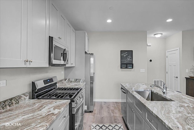 kitchen with white cabinetry, sink, light stone counters, light hardwood / wood-style floors, and stainless steel appliances