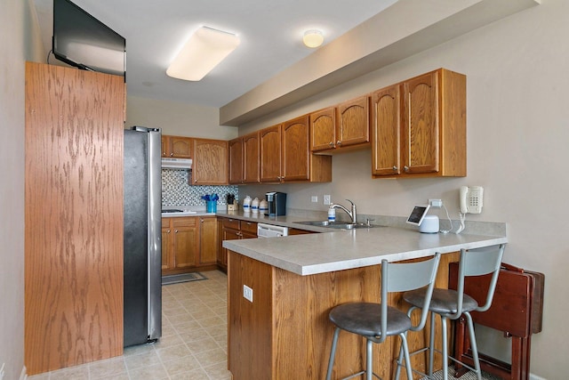 kitchen featuring a breakfast bar, sink, stainless steel refrigerator, kitchen peninsula, and backsplash