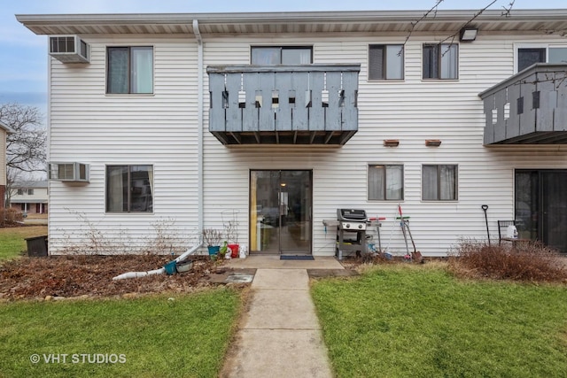 rear view of property featuring a lawn, an AC wall unit, and a balcony