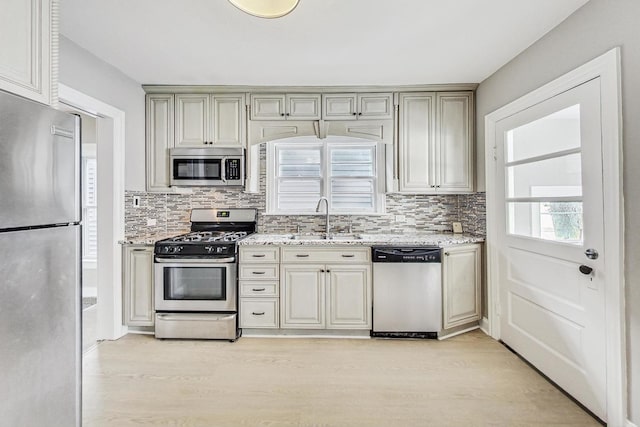 kitchen with stainless steel appliances, sink, decorative backsplash, and light hardwood / wood-style flooring