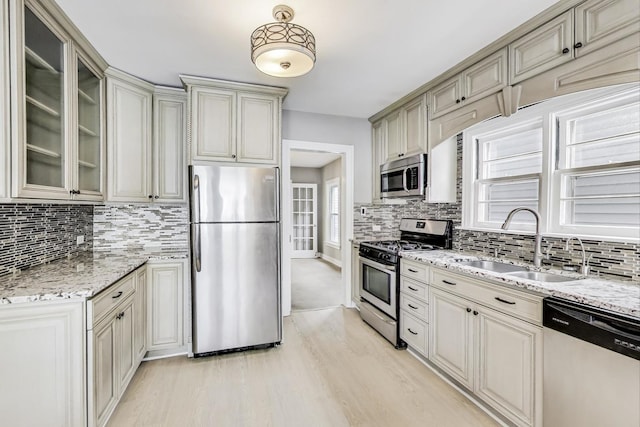 kitchen with sink, stainless steel appliances, light stone counters, light hardwood / wood-style floors, and cream cabinetry