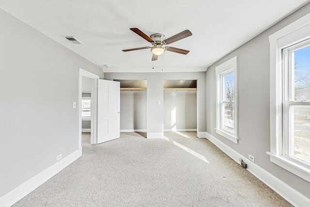 unfurnished bedroom with multiple closets, light carpet, and ceiling fan