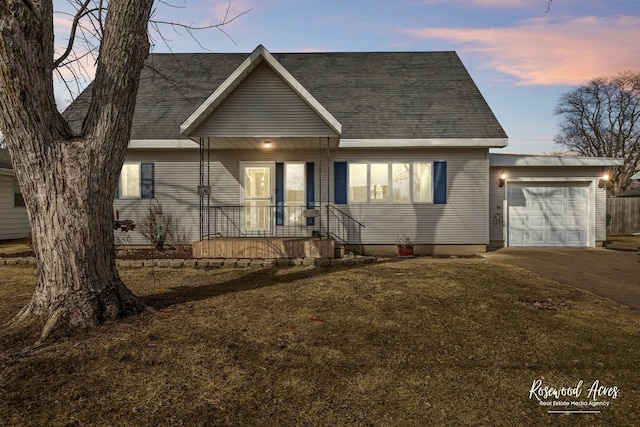 view of front facade featuring a garage, driveway, a lawn, and roof with shingles