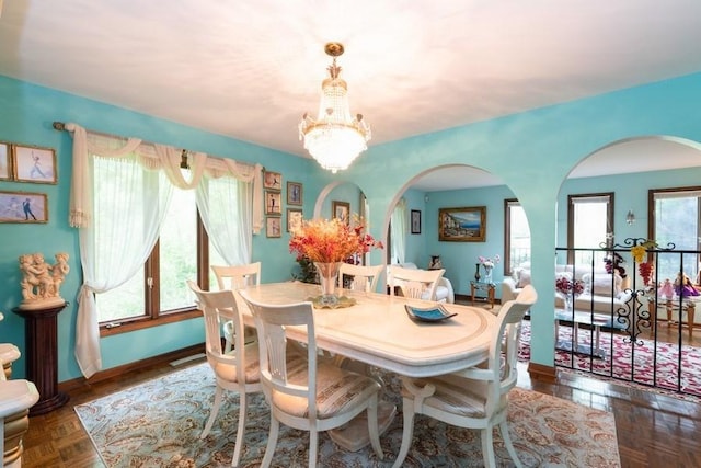 dining space with a healthy amount of sunlight, dark parquet floors, and a notable chandelier