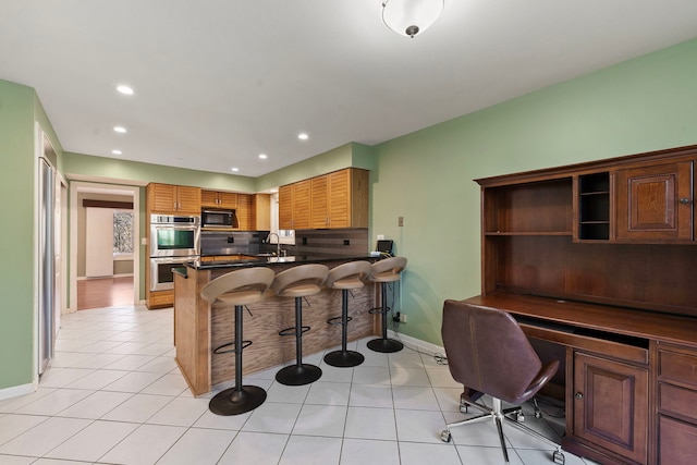 kitchen featuring black microwave, a breakfast bar area, light tile patterned floors, kitchen peninsula, and stainless steel double oven