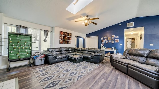 living room with ceiling fan, wood-type flooring, and vaulted ceiling with skylight