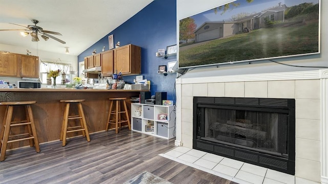 kitchen with a breakfast bar area, vaulted ceiling, a tile fireplace, ceiling fan, and hardwood / wood-style floors