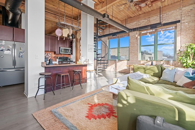 living area featuring brick wall, wooden ceiling, wood finished floors, and a towering ceiling