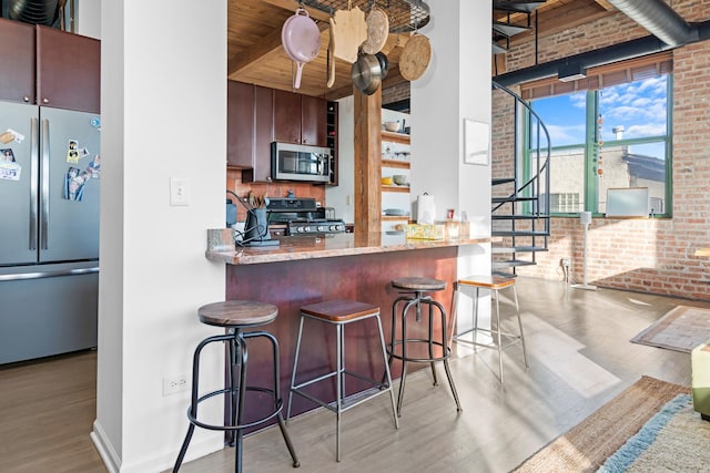 kitchen featuring appliances with stainless steel finishes, a breakfast bar, light wood-type flooring, and brick wall