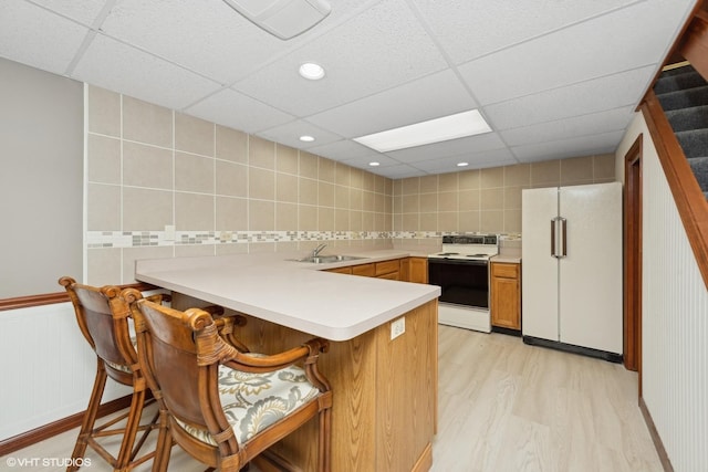 kitchen featuring sink, white appliances, a breakfast bar, kitchen peninsula, and light wood-type flooring