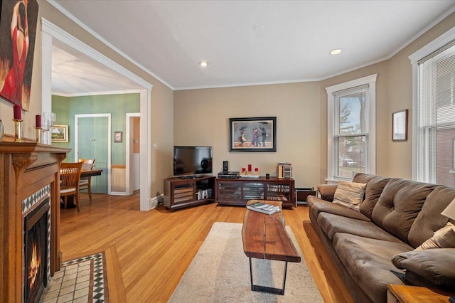 living room featuring a tiled fireplace, light wood-style flooring, recessed lighting, and ornamental molding