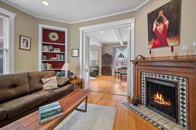 living room with crown molding, a tiled fireplace, beamed ceiling, built in features, and hardwood / wood-style floors