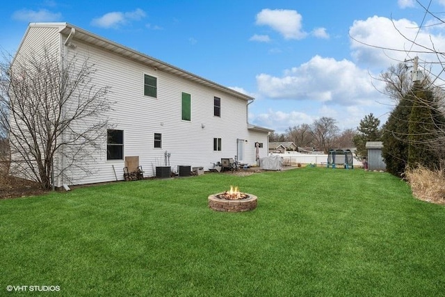 rear view of house featuring cooling unit, a fire pit, and a lawn