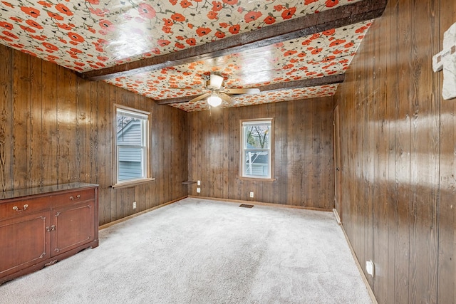 carpeted spare room featuring ceiling fan, wooden walls, and beamed ceiling