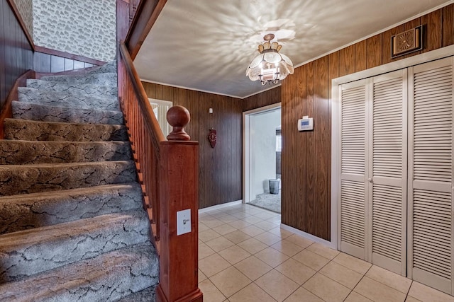 foyer with light tile patterned floors, ornamental molding, a chandelier, and wood walls