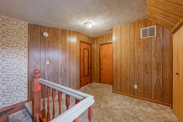 hallway featuring lofted ceiling, light carpet, a textured ceiling, and wood walls