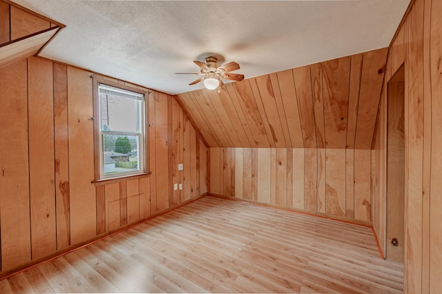 bonus room featuring ceiling fan, vaulted ceiling, light hardwood / wood-style flooring, and wood walls