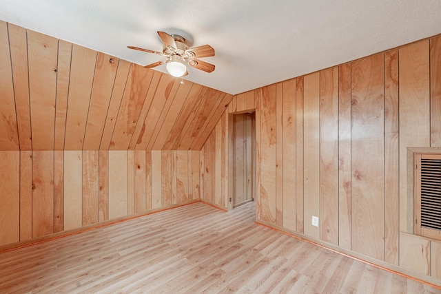 additional living space with lofted ceiling, wooden walls, ceiling fan, and light wood-type flooring