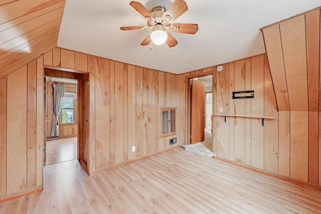 empty room with ceiling fan, wood walls, vaulted ceiling, and light wood-type flooring