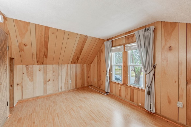 bonus room featuring light wood-type flooring, vaulted ceiling, and wood walls