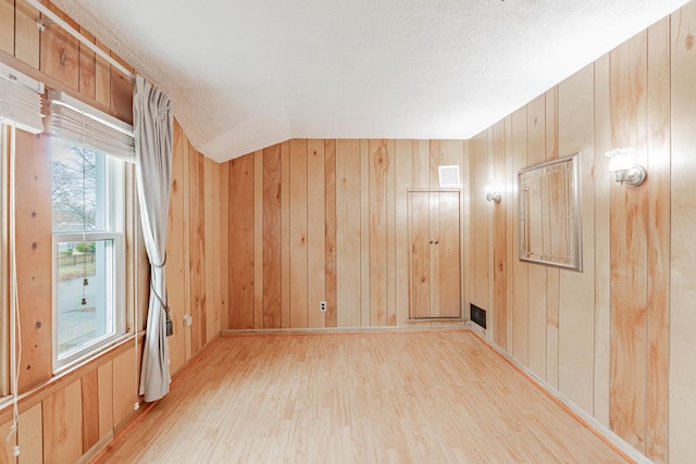 empty room featuring plenty of natural light, light wood-type flooring, and wood walls