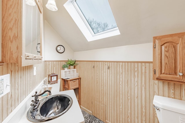 bathroom with lofted ceiling with skylight, sink, wooden walls, and toilet