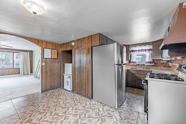 kitchen featuring wooden walls, stainless steel refrigerator, sink, gas stove, and custom range hood