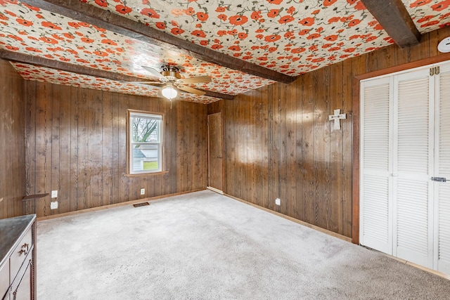 empty room with ceiling fan, carpet flooring, beam ceiling, and wood walls