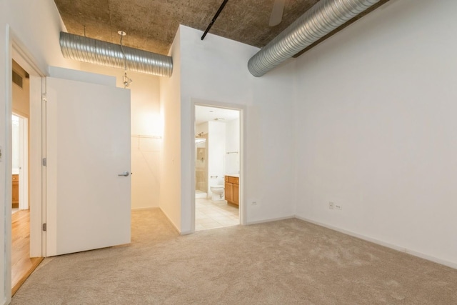 unfurnished bedroom with light carpet, connected bathroom, and a high ceiling