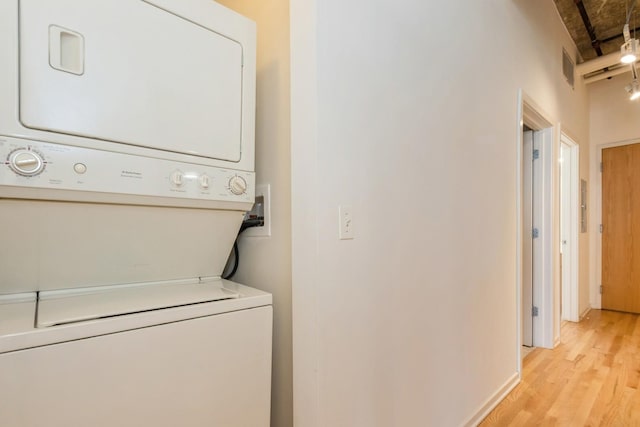 laundry area with stacked washer / dryer and light wood-type flooring