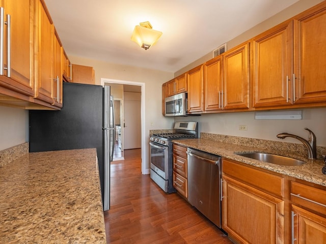 kitchen with stainless steel appliances, wood-type flooring, sink, and light stone counters