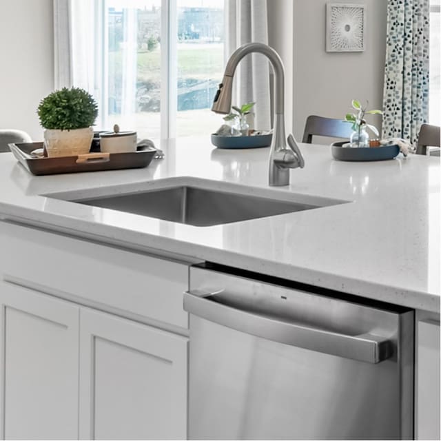 interior details with white cabinetry, stainless steel dishwasher, light stone countertops, and sink