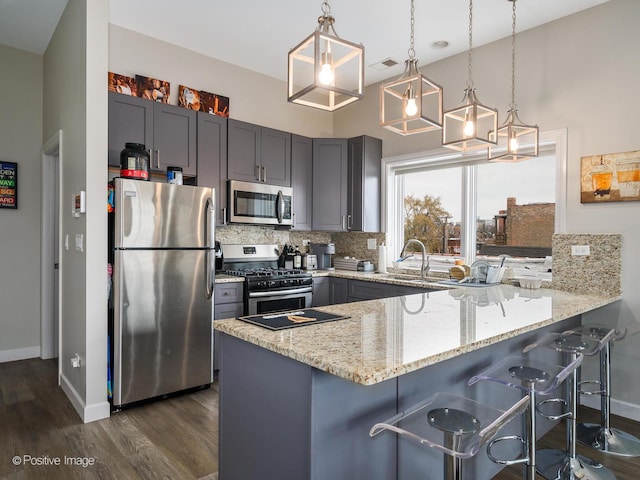 kitchen with pendant lighting, stainless steel appliances, a kitchen bar, decorative backsplash, and kitchen peninsula