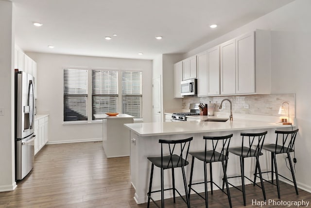 kitchen with appliances with stainless steel finishes, white cabinetry, sink, a kitchen bar, and kitchen peninsula