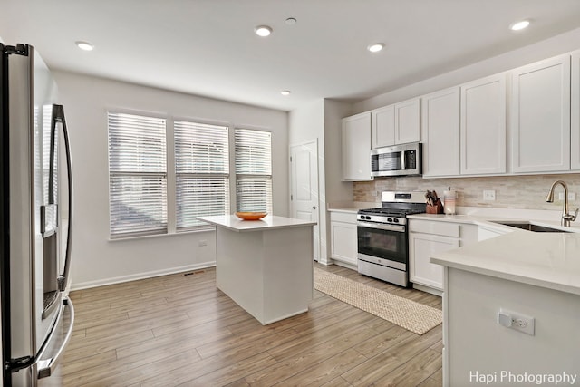 kitchen featuring stainless steel appliances, white cabinetry, a kitchen island, and sink