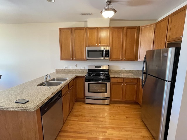 kitchen featuring appliances with stainless steel finishes, pendant lighting, sink, kitchen peninsula, and light hardwood / wood-style flooring